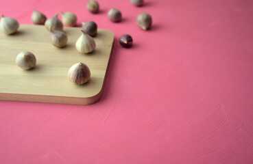 Garlic on cutting board on acrylic scratchy pink canvas background. Food, kitchen, eating photography with copy space.