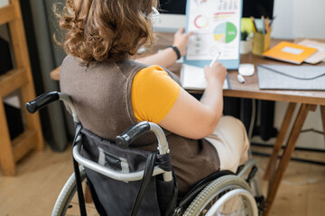Fototapeta na wymiar Back view of young disable economist in wheelchair analyzing financial data