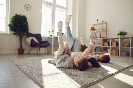 Happy family spending leisure time at home. Carefree, cheerful young mother and children lying on warm floor rug in their apartment. Mum and kids relaxing on soft carpet in cosy sunny living room