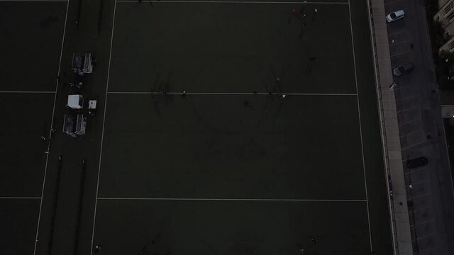 2.7K aerial birds eye view and reveal shot of 6 games of people playing spikeball at night under the floodlights on university soccer field and reveal of skyline