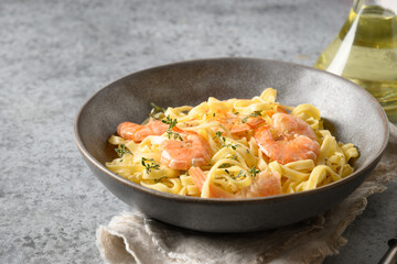 Italian pasta fettuccine with shrimps in bowl on grey table. Close up.