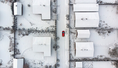 Aerial. Red car driving by the winter village street that goes between the cottages. Top view.