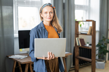 Young beautiful blond businesswoman in casualwear using laptop in office