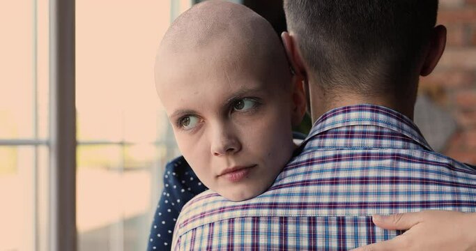 Close up face of bald female cancer patient hugging beloved man, rear back view. Sick woman look at camera smiling hoping for recovery, express gratitude to husband for support and compassion concept