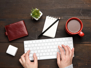 Obraz premium wireless keyboard and two hands are typing on a wooden table, next to a cup with coffee