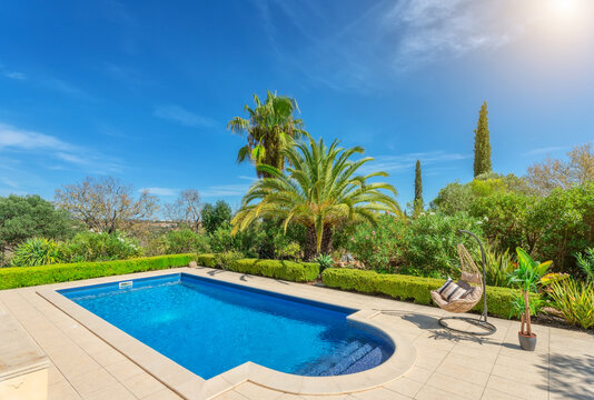 Luxurious pool in the garden of a private villa, hanging chair with pillows for leisure tourists, in summer. Portugal, Algarve.