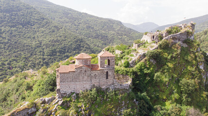Fototapeta na wymiar Medieval Fortress Asen , on a hill in eastern Europe, Bulgaria. Bulgarian antique and heritage stronghold fortification on a rock. Aerial view of a holy place and monastery. Tourist place with forest.