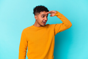 Young african american curly man isolated on blue looking far away keeping hand on forehead.
