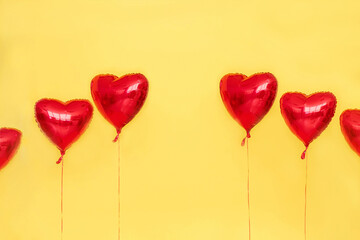 Red foil balloons in shape of heart isolated on yellow background. Mockup for design. Celebrating Valentines Day. Holiday, greeting, romantic, love, birthday, concept. Womens day. Close up, copy space