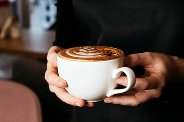 Spicy cappuccino with star anise and cinnamon in hands of barista.