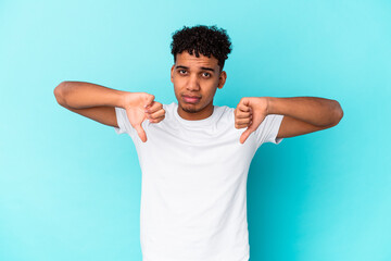 Young african american curly man isolated on blue showing a dislike gesture, thumbs down....