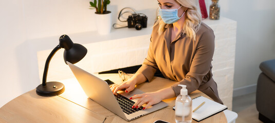 Woman with face mask working in office with laptop and using hand alcohol gel or sanitizer against...