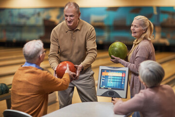 Fototapeta premium Group of senior people playing bowling together while enjoying active entertainment at bowling alley, copy space
