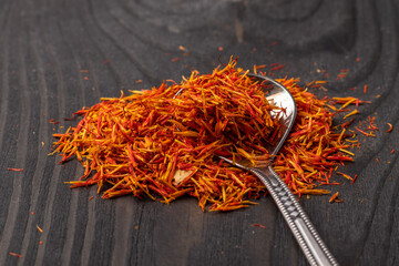 A pile of saffron stigmas with a melchior spoon on a dark wooden background