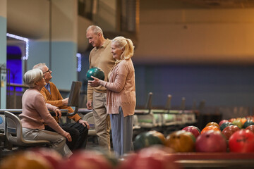 Wide angle side view at group of senior people playing bowling together while enjoying active entertainment at bowling alley, copy space - obrazy, fototapety, plakaty