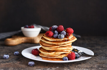 Delicious homemade pancakes in a plate with berries: raspberries, blueberries and maple syrup on a concrete background. With copy space.