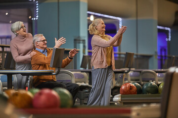 Side view at group of senior people playing bowling together while enjoying active entertainment at bowling alley, copy space