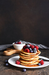 Delicious homemade pancakes in a plate with berries: raspberries, blueberries and maple syrup on a concrete background. With copy space.