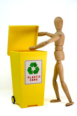 Small wooden mannequin, near the yellow separate collection bin, on a white background