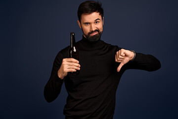 Young handsome man drinking bottle of beer standing over isolated Pacific Blue background with angry face, negative sign showing dislike with thumbs down, rejection concept