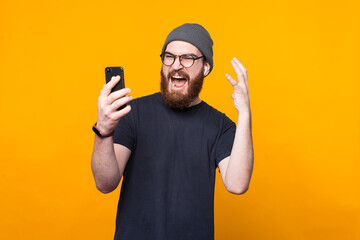 Photo of bearded hipster man looking angry at smartphone.