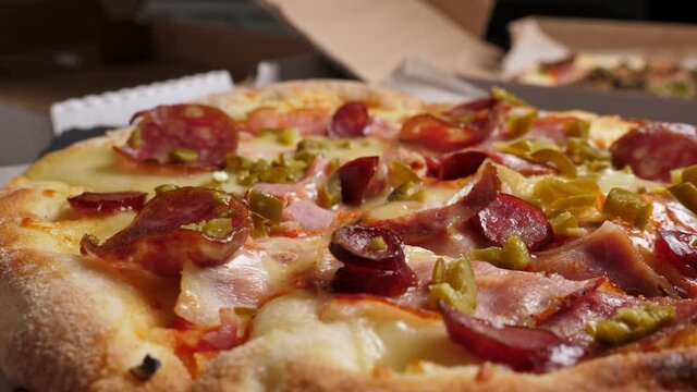 One salami and bacon pizza rotating on boxes with pizza background, closeup