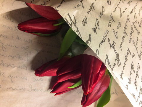 Bouquet of red tulips in paper wrap with inscriptions in flower store, birthday gift, Valentine's Day, March 8. Top view, space for text. High quality photo
