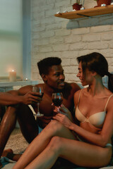 In love. Young beautiful african couple, half naked man and woman drinking wine and talking while sitting on the bed at home