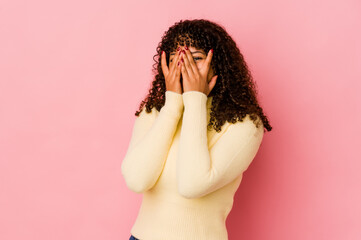 Young african american afro woman isolated blink at the camera through fingers, embarrassed covering face.