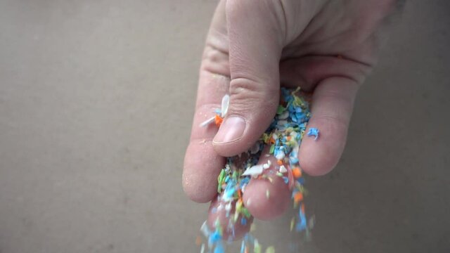 Side view of micro plastics falling from a human hand. Slow-motion of waste non-recyclable plastic.  Selective focus on the hand. Environmental issues, global warming, and climate change concept.