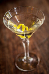 Martini cocktail alcohol drink beverage with lemon twist and bokeh background on a wooden table