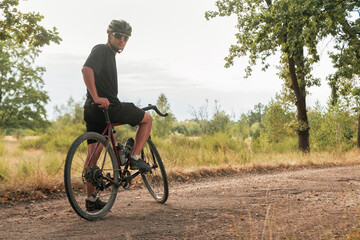 Obraz premium Cyclist stands with a bicycle on a gravel road in the countryside.