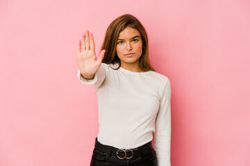 Young skinny caucasian teenager girl standing with outstretched hand showing stop sign, preventing you.