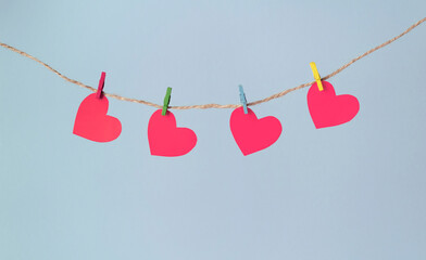 Paper hearts hang on clothespins on a rope on a pastel blue background.