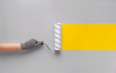 Girl in a glove paints a yellow strip with a paint roller on a gray wall.