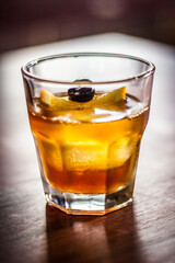 Dark n stormy cocktail alcohol drink beverage with lemon slices black olive ice and bokeh background