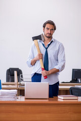 Young male furious employee holding hatchet in the office