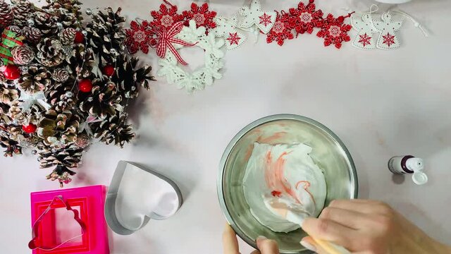 The pastry chef dyes the cake cream. Preparing ingredients for baking. Mix the cream with a silikon paw. New Year's decor on the table.