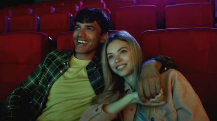 Portrait of cheerful couple, young man and woman smiling, holding hands while having romantic movie date at the cinema