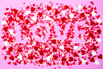 The word Love in capital letters spelled out on a pink background using colorful sugar-coated smarties
