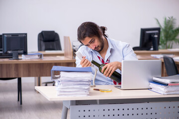 Young male employee drinking alcohol in the office