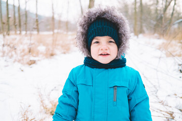 Little baby boy in winter wear and knitted hat on snowy nature background. Cute child looking to camera. Family, son, love concept.