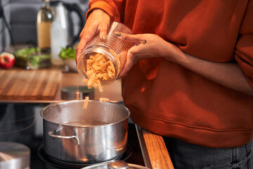 Woman pouring pasta at the pan while preparing dinner
