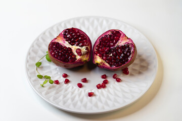 Fototapeta na wymiar Two halves of fresh ripe pomegranate on a white plate, close-up..