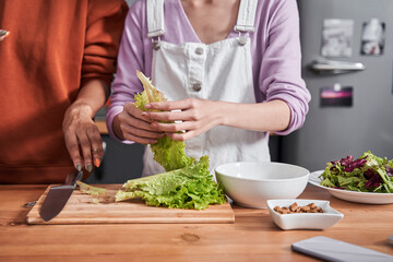 Woman chopping salad at the wooden plank at the table
