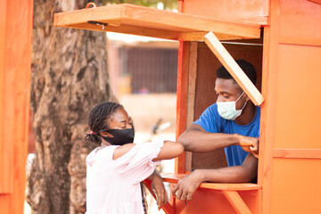 man who runs a pos cash withdrawal service and a female customer touch elbows as greeting, both wearing face masks