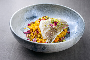 Modern style traditional sauteed skrei cod fish filet with skin in a bed of Persian jeweled saffron rice pilaw served in ceramic design bowl as close-up