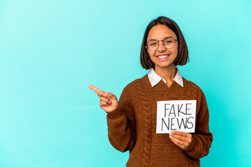 Young hispanic mixed race woman holding a fake news placard smiling and pointing aside, showing something at blank space.