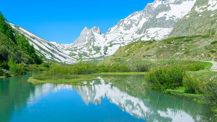 Fototapeta na wymiar Mountains peaks mirroring in the lake showing symmetry. Mountains are full of snow and the water is calm. Val Veny, Italy