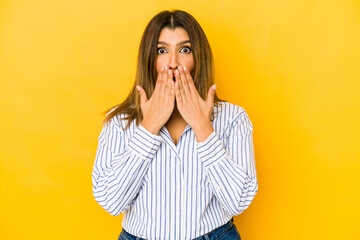 Young indian woman isolated on yellow background shocked covering mouth with hands.
